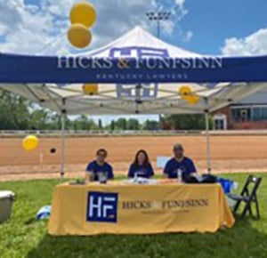 Hicks & Funfsinn legal team sitting under firm's banner and tent at the Bluegrass Scavenger Hunt for Kids’ Sake event
