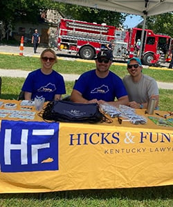 Hicks & Funfsinn legal team members sitting at firm's table at The Nest’s Family Fun Day event